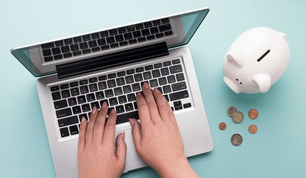 woman typing IT support costs on laptop with piggy bank